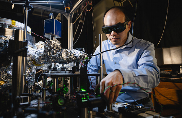 Prof. Tongcang Li and an optical setup for studying the coupling between spin qubits and the mechanical rotation of a levitated particle. Photo by Charles Jischke.
